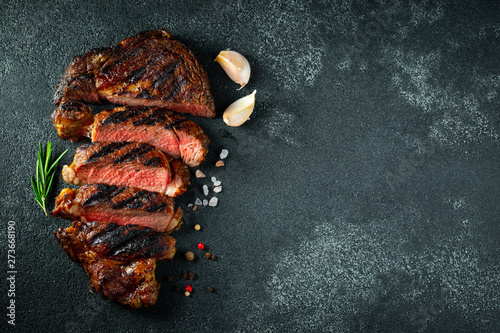 Sliced steak ribeye, grilled with pepper, garlic, salt and thyme on a dark stone background. Top view. Flat lay