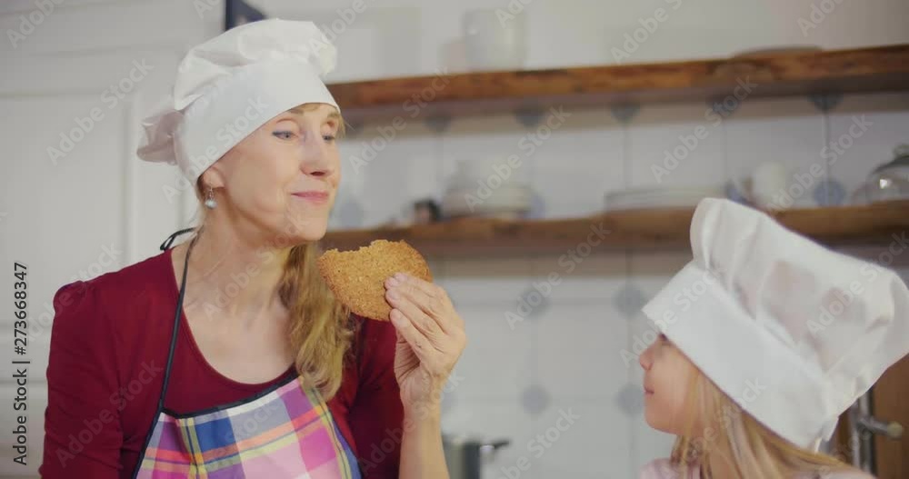 Close up of grandmother that tastes cookies baked with a help of her granddaughter and praises her