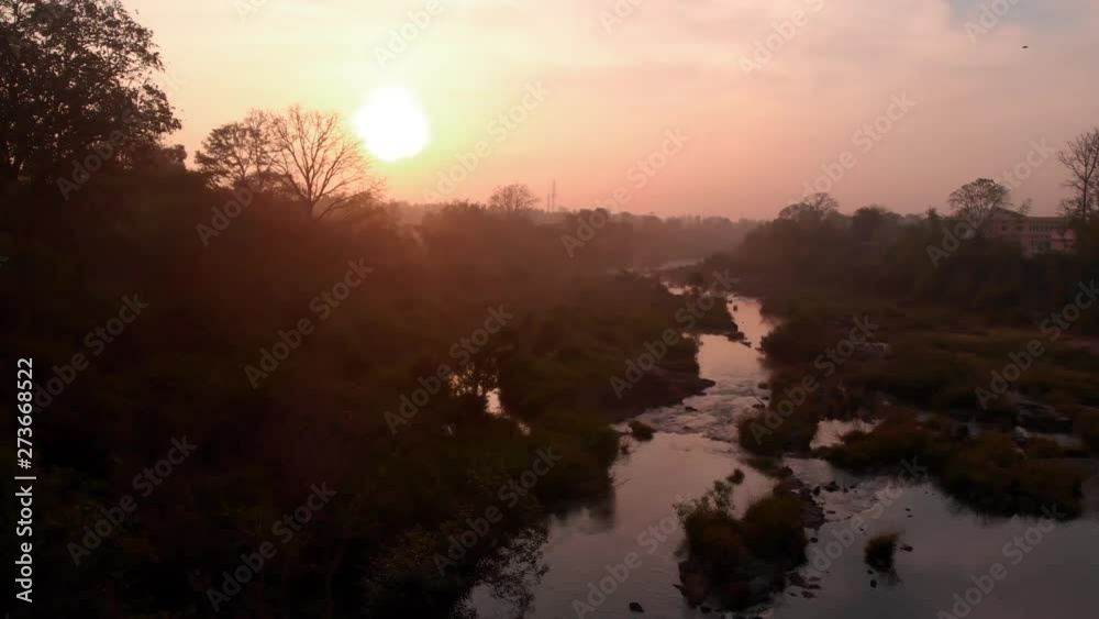Drone moving forwards and upwards towards a rising sun with a foreground of river
