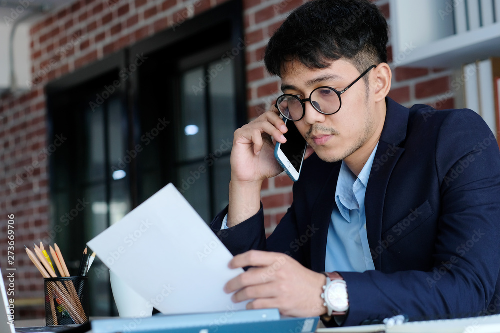 Young asian businessman reading papers talking phone at office, business communication and technology concept Young asian businessman reading papers talking phone at office, business communication and technology concept