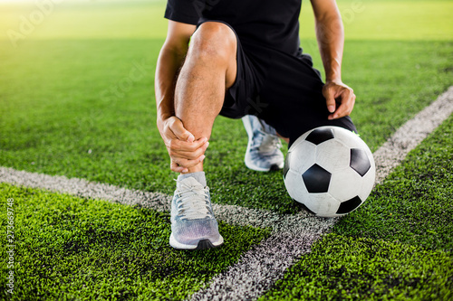 Soccer ball on green artificial turf with footballer is sitting and catch the ankle