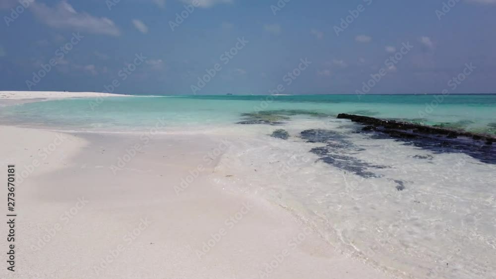 Small waves dashing on a white sand beach and some small rocks in the Maldives Islands. Camera slowly moves to he blue sky with some scattered clouds in the distance Small waves dashing on a white sand beach and some small rocks in the Maldives Islands. Camera slowly moves to he blue sky with some scattered clouds in the distance