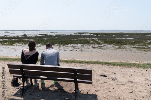 young couple sitting on beach bench in summer sea background low tide