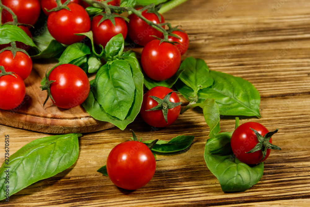 Fresh cherry tomatoes with green basil leaves on a wooden table Fresh cherry tomatoes with green basil leaves on a wooden table