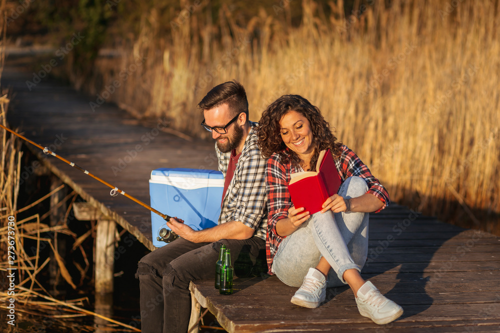 Couple fishing and reading at the lake docks