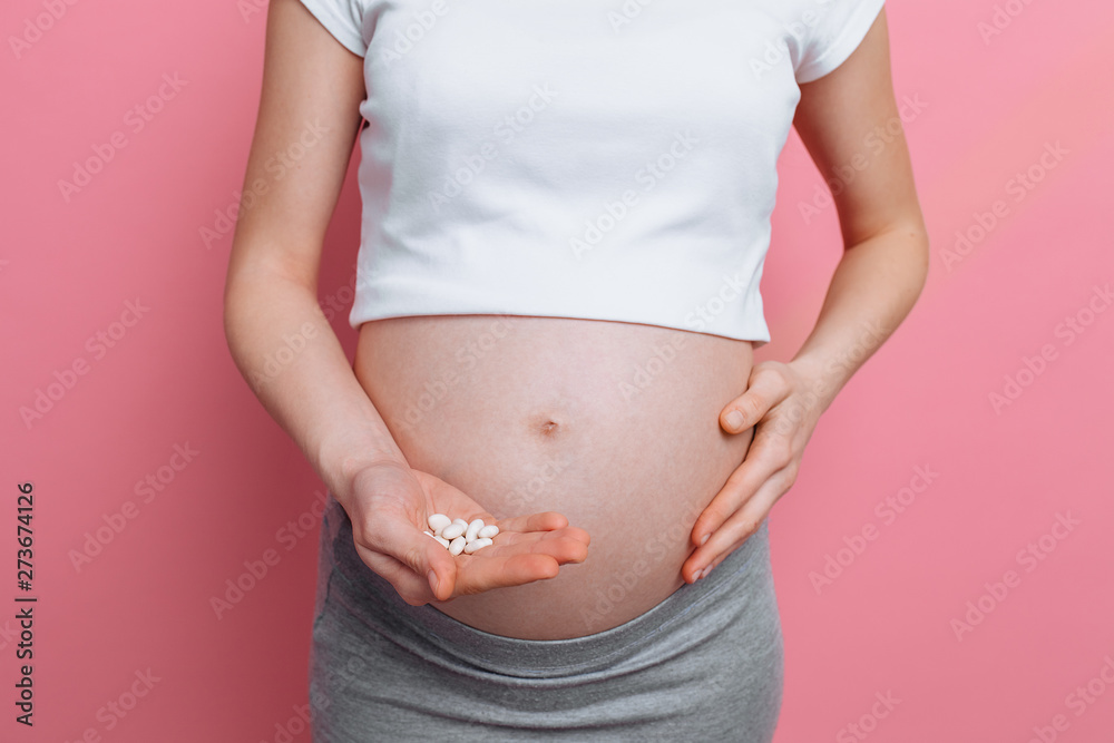 Stomach of a pregnant woman holding round white pills for health care, close-up of the human body without a face Stomach of a pregnant woman holding round white pills for health care, close-up of the human body without a face