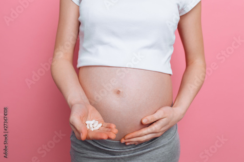 Stomach of a pregnant woman holding round white pills for health care, close-up of the human body without a face © Shopping King Louie