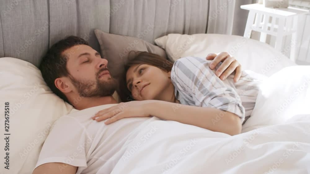 Handheld shot of affectionate young woman in pajama waking up and kissing her boyfriend in morning. They are smiling and caressing each other Handheld shot of affectionate young woman in pajama waking up and kissing her boyfriend in morning. They are smiling and caressing each other