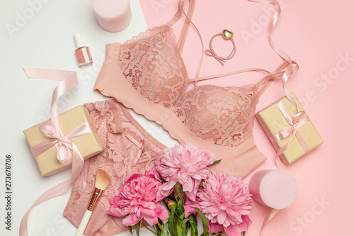 Female elegant pink lace bra and panties, pink candles, hair tie, a bouquet of beautiful peonies, nail polish, jewelry, top view