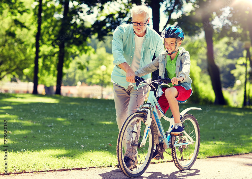Obraz premium family, generation, safety and people concept - happy grandfather teaching boy how to ride bicycle at summer park