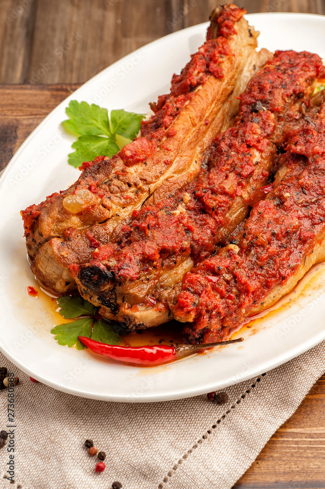 Grilled pork ribs in spicy sauce with tomatoes. Ketogenic and paleo food. Large portion on a white plate. Close up and vertical orientation. . Grilled pork ribs in spicy sauce with tomatoes. Ketogenic and paleo food. Large portion on a white plate. Close up and vertical orientation. .