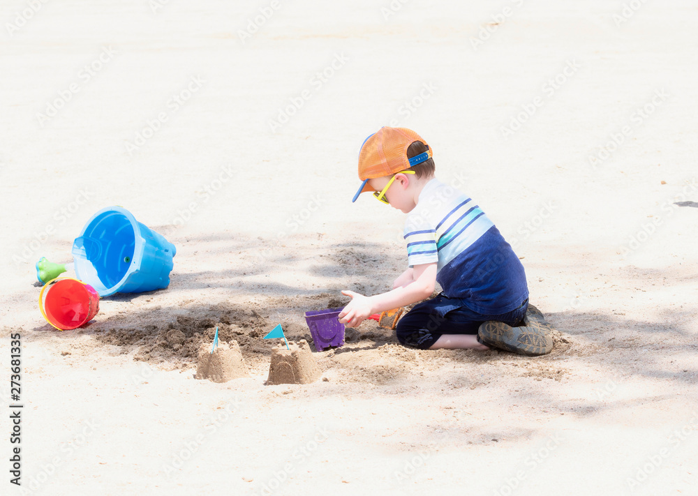 Toddler with Hat & Sunglasses Plays on a Sandy Beach with Buckets Building Sand Castles Toddler with Hat & Sunglasses Plays on a Sandy Beach with Buckets Building Sand Castles