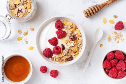 Greek yogurt in bowl with raspberries, honey and muesli on white stone table top view. Healthy diet breakfast.