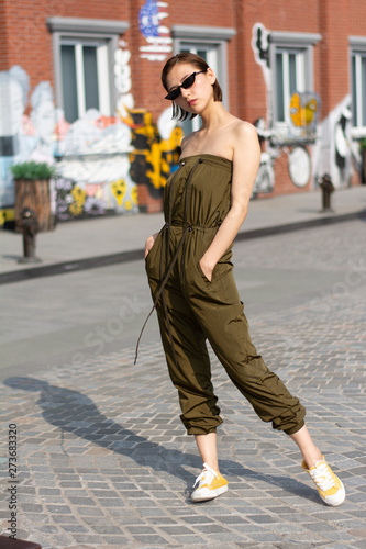 Asian Chinese model girl influencer street shot. Wearing army green color jumpsuit. Street Graffiti background.