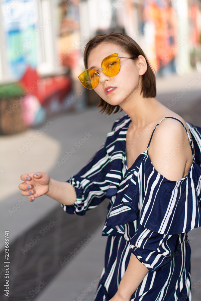 Fototapeta premium Asian Chinese model girl influencer street shot. Wearing black striped dress. Street Graffiti background.