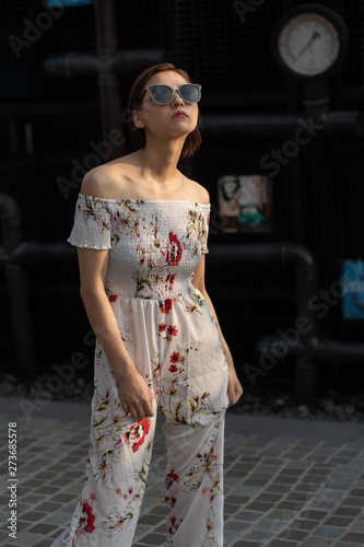 Asian Chinese model girl influencer street shot. Wearing white printed floral patterned jumpsuit.  Street view background.