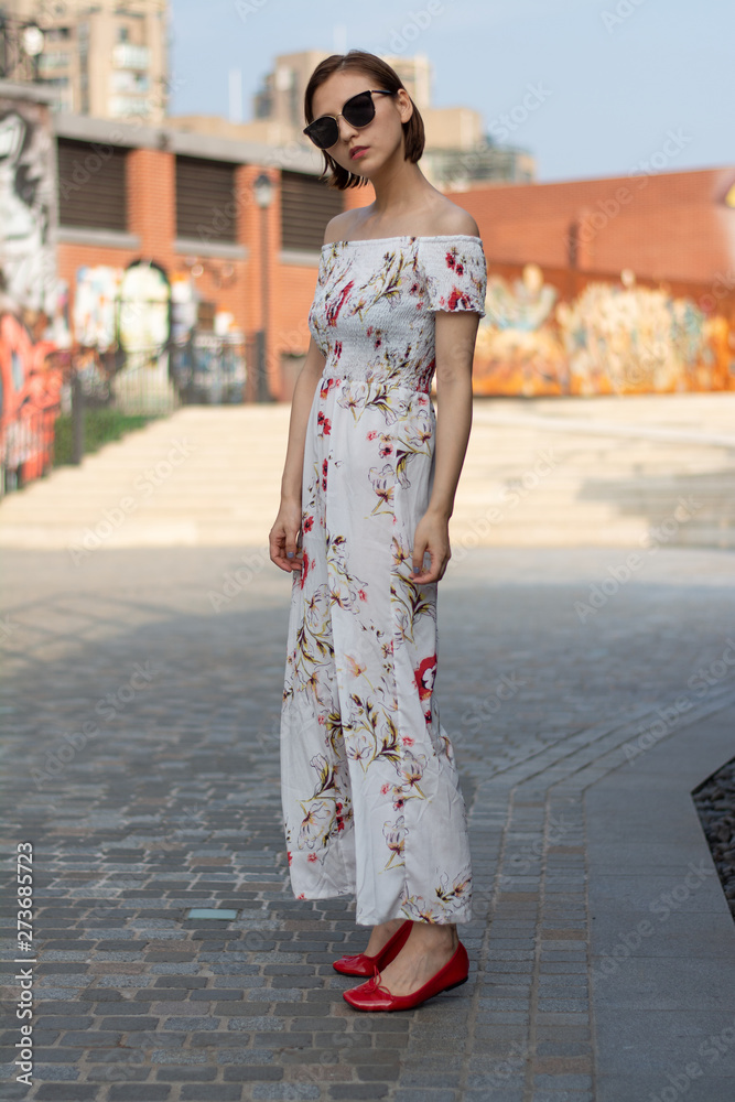 Asian Chinese model girl influencer street shot. Wearing white printed floral patterned jumpsuit.  Street view background.