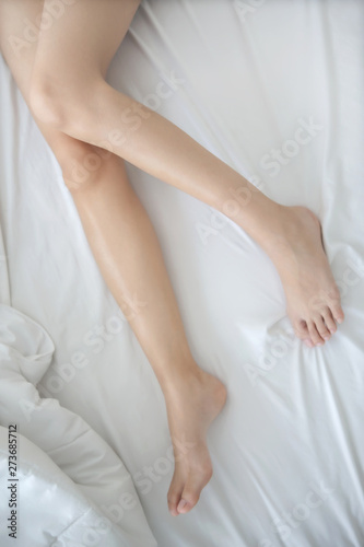 Slim and silky smooth woman legs lying on the bed with white bedclothes in the morning light