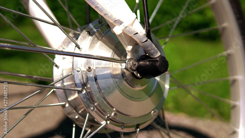 Wheel of the electric bicycle front view in sunny summer day with green grass bokeh on the background. E bike motor with light reflections. Close up.