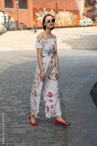 Asian Chinese model girl influencer street shot. Wearing white printed floral patterned jumpsuit.  Street view background.