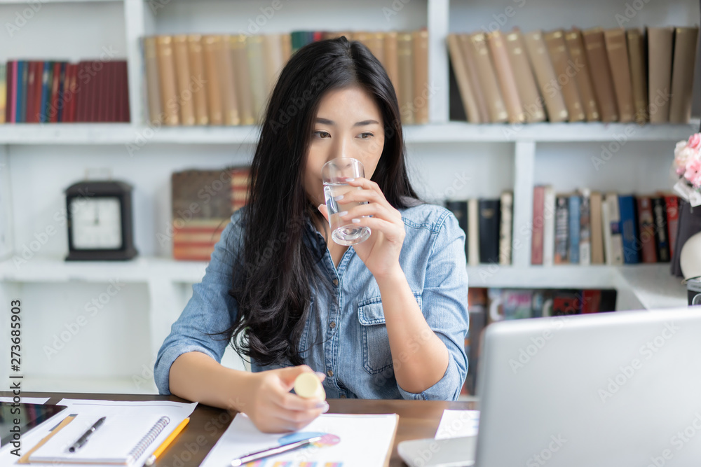 Young Thai girl Business woman taking medicine and drinking water,holding pills ,glass of water at workplace,she working hard with laptop while feels sick,medicine,health care Medical people concept Young Thai girl Business woman taking medicine and drinking water,holding pills ,glass of water at workplace,she working hard with laptop while feels sick,medicine,health care Medical people concept