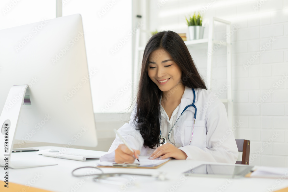 Asian female doctor sitting at hospital office desk giving all patient convenience online service advice and smiling write a prescription to order medical, health care and preventing disease concept. Asian female doctor sitting at hospital office desk giving all patient convenience online service advice and smiling write a prescription to order medical, health care and preventing disease concept.