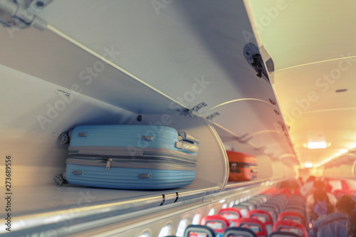 Carry-on luggage on the top shelf over head on airplane, passenger put bag cabin compartment air craft business class,vintage color,copy space photo