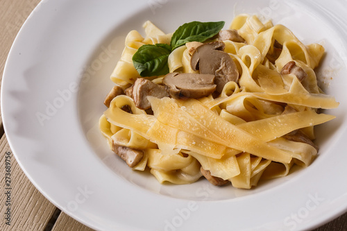 Tagliatelle vegetarian Pasta Dish with Mushrooms decorated with basil. Delicious lunch with pasta and white mushrooms. On wooden background.