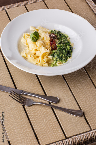 Tagliatelle vegetarian Pasta Dish with spinach and dried tomatoes decorated with basil. Delicious lunch with pasta and spinach. On wooden background. photo