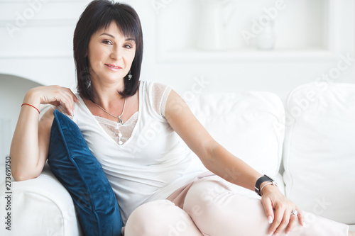 Attractive adult woman sitting on the couch indoors. Beautiful middle-age female at home. Portrait of 35-40 years woman. Free Download Attractive adult woman sitting on the couch indoors. Beautiful middle-age female at home. Portrait of 35-40 years woman. - GFXLoad