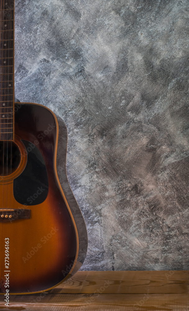 Acoustic guitar resting against on wooden table a blank cement wall background with copy space, relaxing time and playing music for holidays in the home.