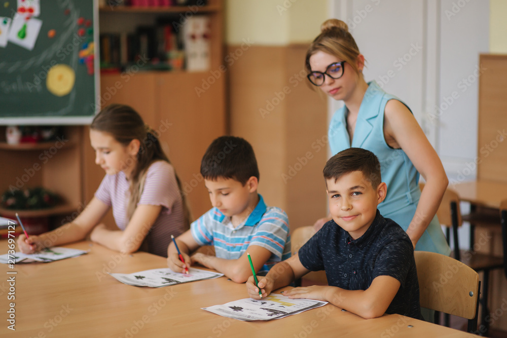 Fototapeta premium Teacher helping school kids writing test in classroom. education, elementary school, learning and people concept