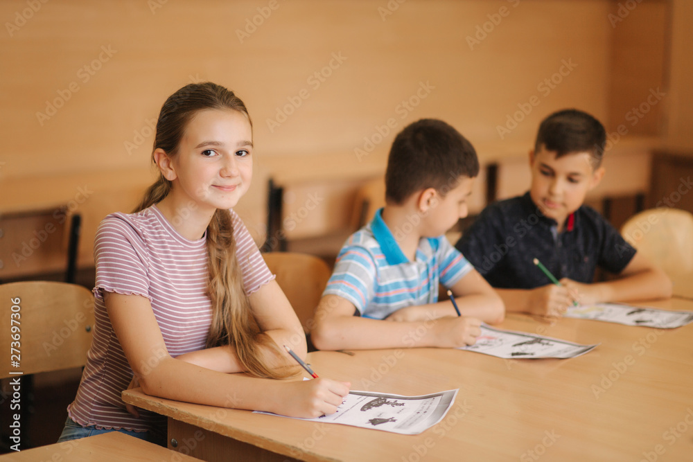 Education, elementary school. Learning and people concept - group of school kids with pens and notebooks writing test in classroom Education, elementary school. Learning and people concept - group of school kids with pens and notebooks writing test in classroom