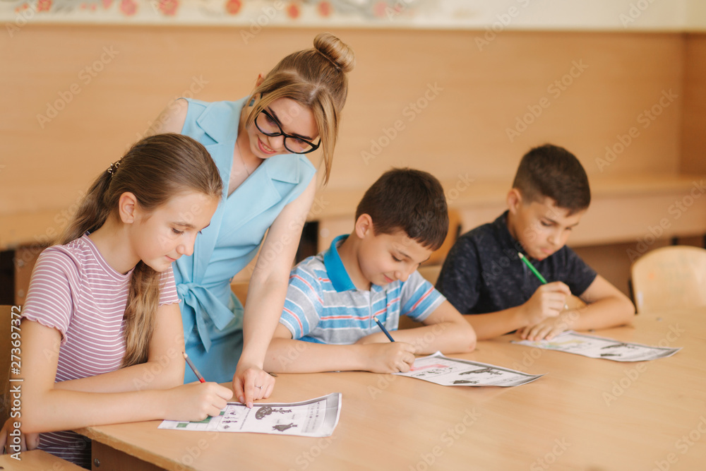 Teacher helping school kids writing test in classroom. education, elementary school, learning and people concept Teacher helping school kids writing test in classroom. education, elementary school, learning and people concept