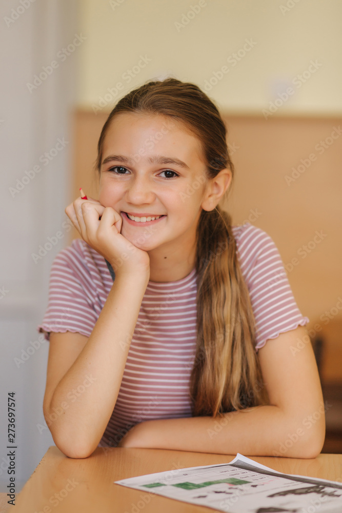 Happy schoolgirl sitting at desk and writing in exercise book Happy schoolgirl sitting at desk and writing in exercise book
