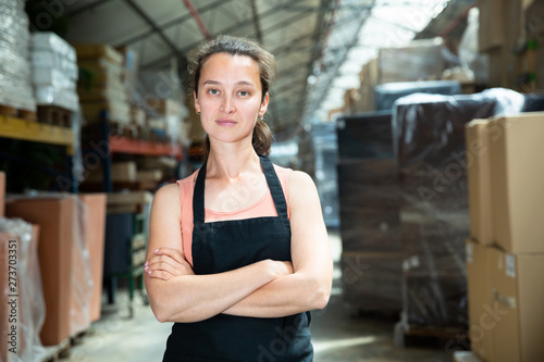 Portrait of female worker in apron with arms crossed standing in warehouse