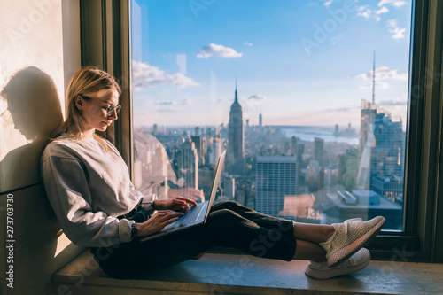Photography Concentrated female freelancer keyboarding information on laptop computer working remote in coworking office with panoramic views of scenic Manhattan downtown