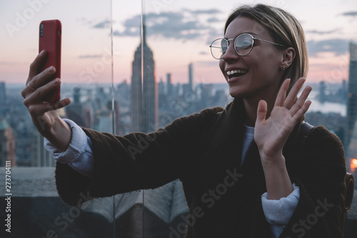 Canvas Print Happy caucasian hipster girl saying Hello to her followers in travel blog while visiting famous landmark place with scenery view of New York cityscape