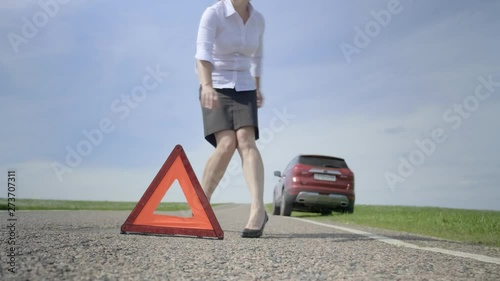 woman sets up emergency stop sign on road and returns to car. Closeup, blurred background. girl installs red triangular warning signal. photo