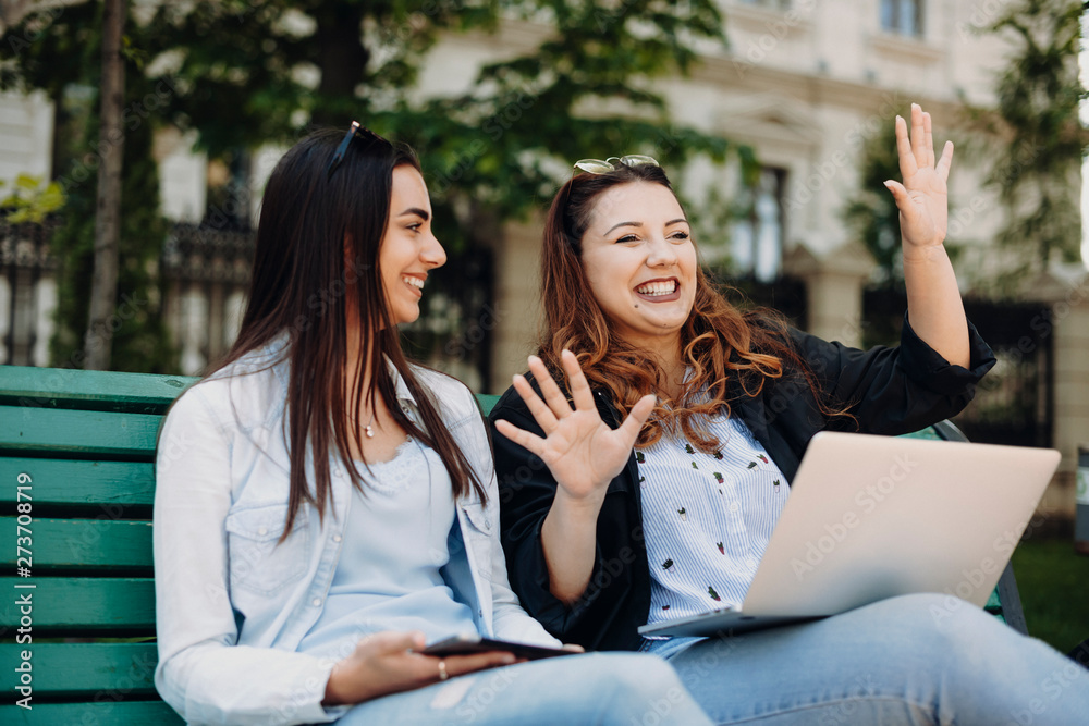 Beautiful plus size women with long dark hair laughing while storytelling to her girlfriend sitting on a bench outside against a building. Beautiful plus size women with long dark hair laughing while storytelling to her girlfriend sitting on a bench outside against a building.