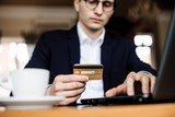 Hands of a young man holding a gold credit card and working at laptop dressed in suit sitting at a desk.
