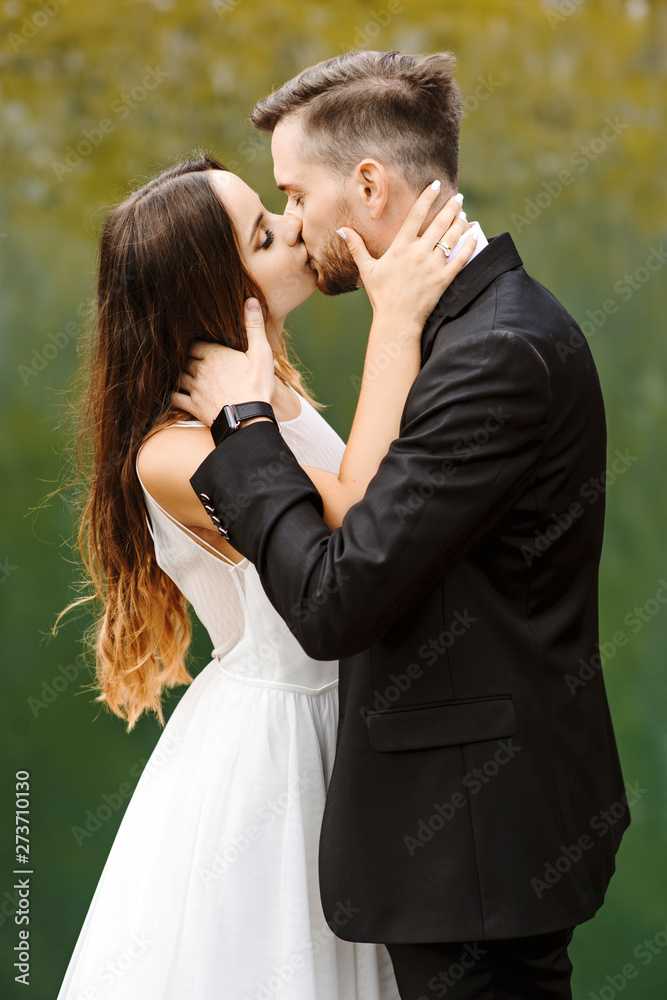 Portrait of a lovely young bride and groom kissing at the edge of a lake against lake reflection. Portrait of a lovely young bride and groom kissing at the edge of a lake against lake reflection.