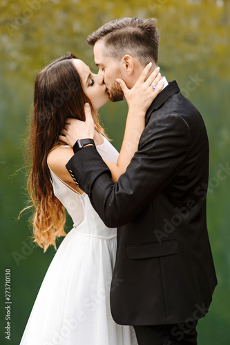 Portrait of a lovely young bride and groom kissing at the edge of a lake against lake reflection. © Strelciuc