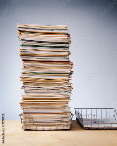 In, out trays on desk with tall stack of never ending office paperwork