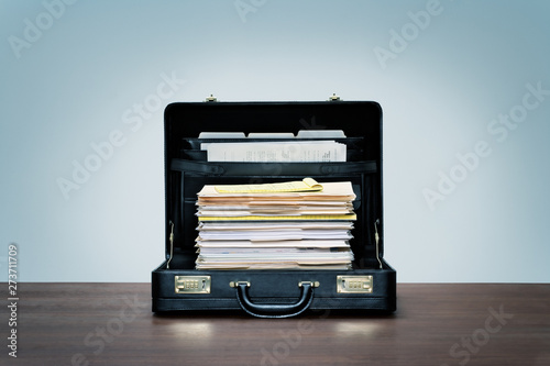 Tall stack of files and folders in black leather briefcase on wood desk with blue background. photo