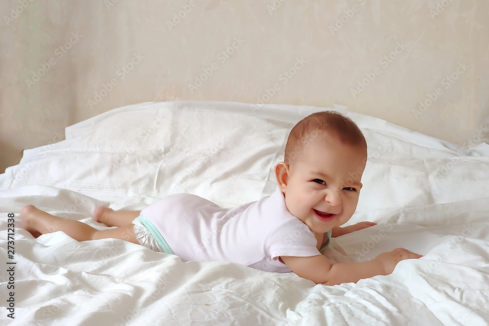 A very happy baby is lying on a white bed on his stomach. A very happy baby is lying on a white bed on his stomach.