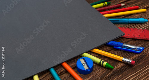 Many different stationery on a wooden surface under a dark gray sheet of paper. Flat lay. Gray empty space for text. Back to school supplies. Office tool. 