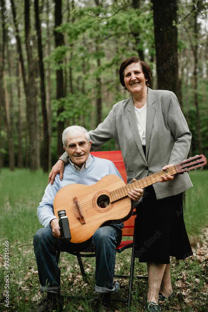 Loving mature couple coming on picnic with guitar. Happy senior couple playing a guitar and having a romantic date outdoor. Happy senior people spending time together on spring field. 