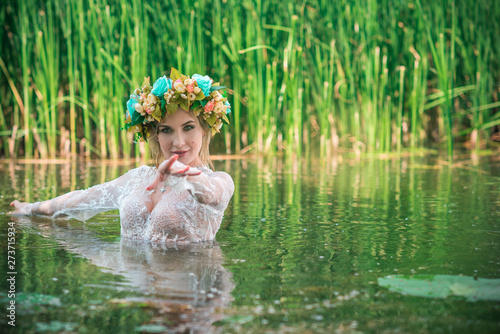 Fototapeta Naklejka Na Ścianę i Meble -  A fabulous, lake nymph in long white lace dress and wreath. Artistic Photography, Mysterious scene. European Witch . Fairytale
