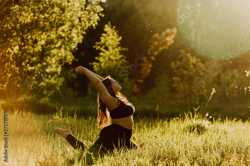 Beautiful plus size girl doing yoga in nature on a sunny summer day. Body positive, sports for women, harmony, asana, healthy lifestyle, inspiring look, self-love and wellness.